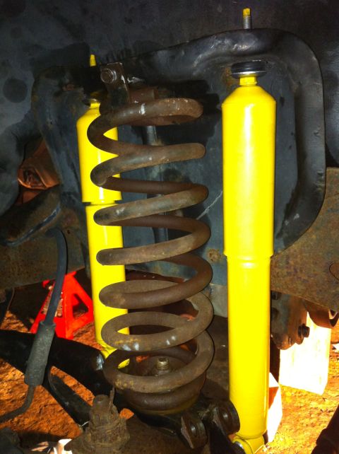 1992 Ford Bronco - This image shows a rusty coil spring and two bright yellow shock absorbers, likely part of a vehicle's suspension system.