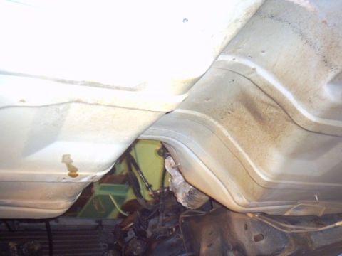 1991 Ford LTD Crown Victoria - Underside view of a white car's floor pan and rocker area showing surface rust staining, a gap where the pan meets the frame rail and a tor…