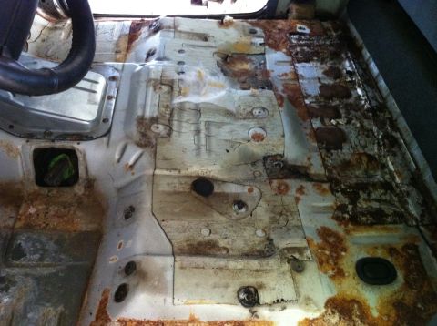 1992 Ford Bronco - The interior floor of a vehicle shows significant rust and corrosion, with a partial view of the steering wheel.