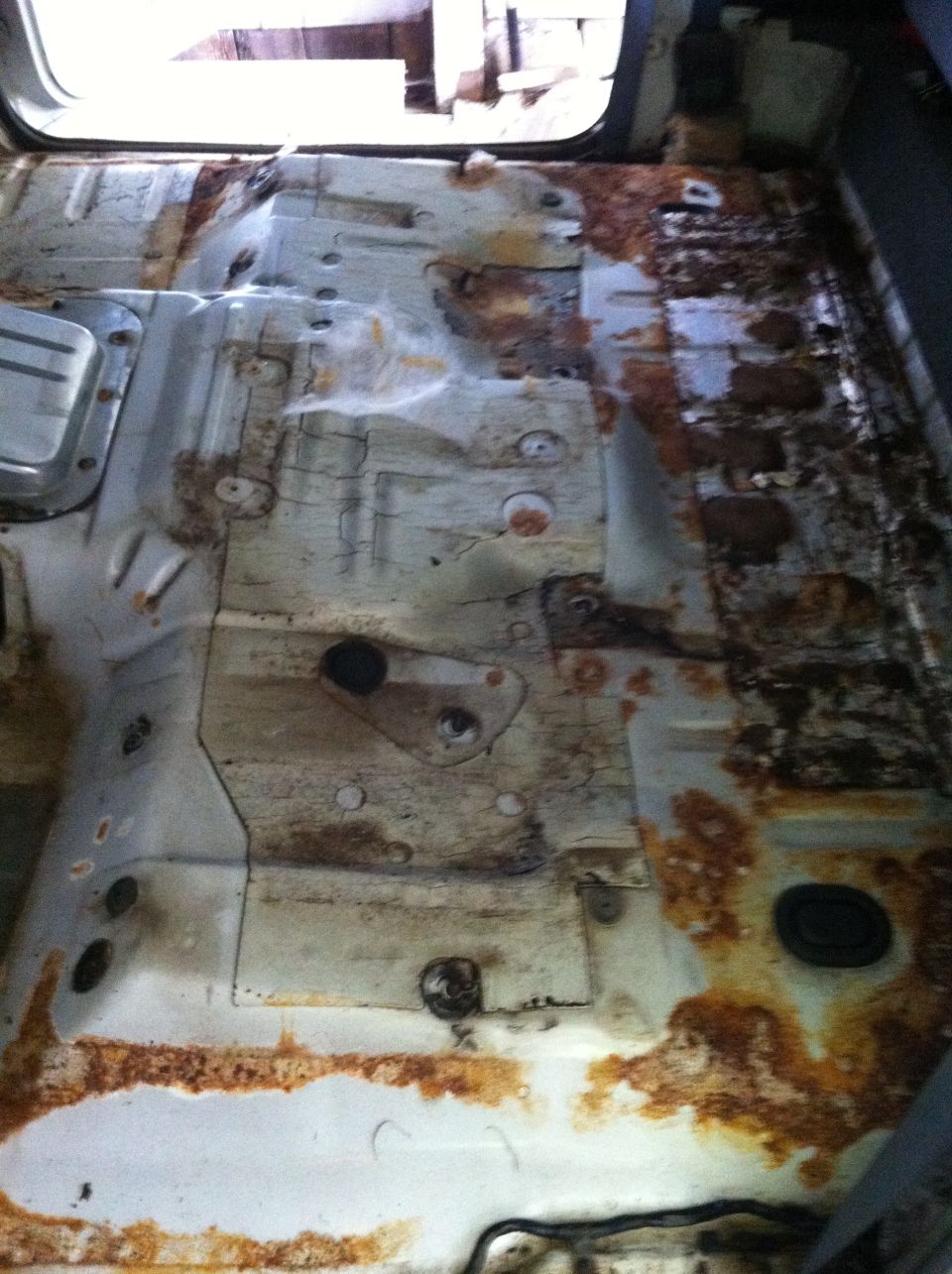 Rusted interior floor pan with visible mounting points and rubber grommets
