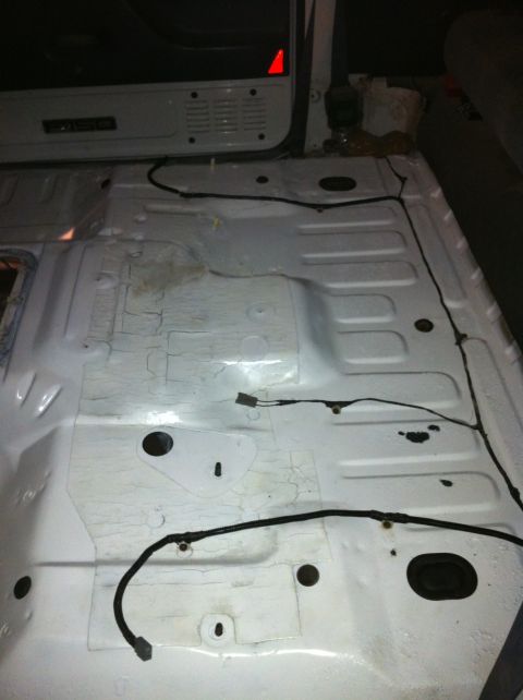 1992 Ford Bronco - The interior floor of a vehicle, stripped down to reveal the metal and wiring beneath. A 'F150' badge is visible on the interior paneling.