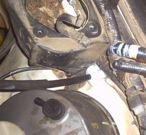 1991 Ford LTD Crown Victoria - Under-hood close-up at the cowl showing a white nylon harness grommet or bulkhead fitting passing wiring loom through the firewall, with bl…