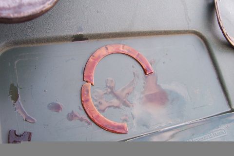 1980 Ford Bronco - A close-up view of a damaged copper washer resting in a container, possibly during a repair or maintenance process.