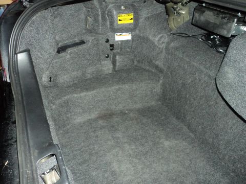 2004 Mercury Grand Marquis - The carpeted interior of a car's trunk shows some wiring and a warning label on the wall.