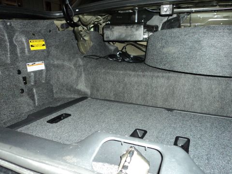 2004 Mercury Grand Marquis - The interior of a car trunk shows carpeting and a spare tire well with visible wiring and a black box.