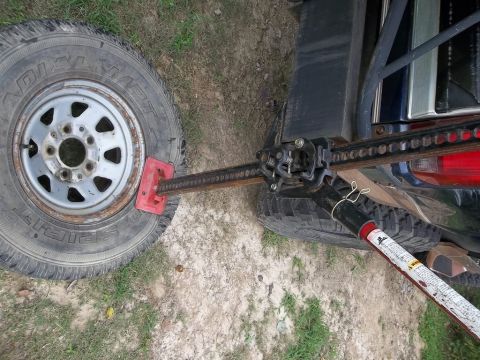 1995 Ford Bronco - A high-lift jack is being used to lift a vehicle's tire, with the spare tire and part of the vehicle body in view.