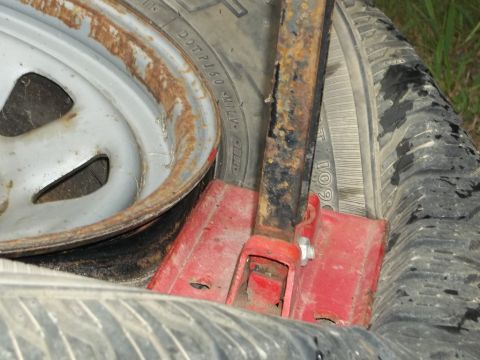 1995 Ford Bronco - A car jack is positioned on tires, showing signs of rust on its metal components and the wheel rim.
