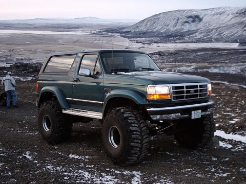 1996 Ford Bronco - Modified 1996 Ford Bronco sits on a rocky terrain with snow-capped mountains in the background.