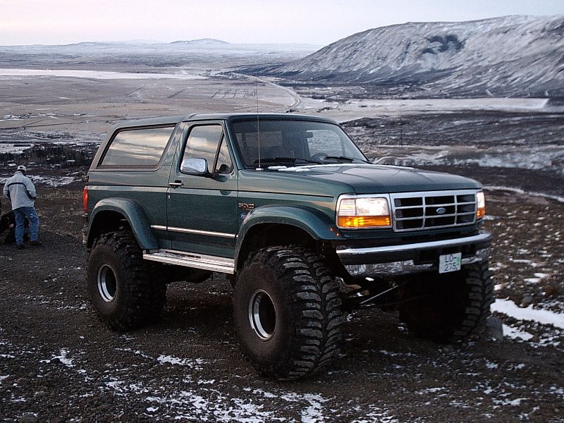 Lifted dark green Ford Bronco on big mud tires atop a snowy hill