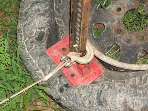 1995 Ford Bronco - A hi-lift jack is positioned on a red base, connected to a wire rope, and placed on a tire.