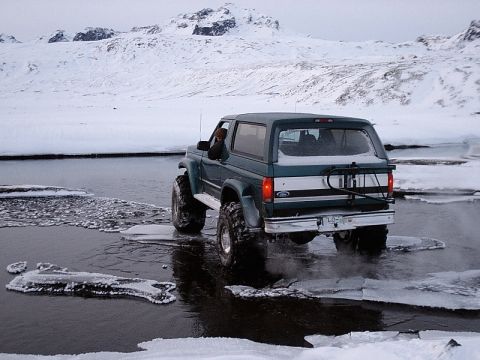 1996 Ford Bronco - A green Ford Bronco navigates through a partially frozen body of water with snow-covered mountains in the background.