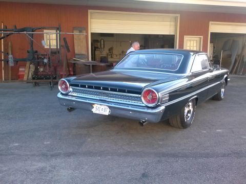 1960 Ford Falcon - The rear of a black 1963 Ford Galaxie 500 coupe is shown parked in front of a garage with the doors open.