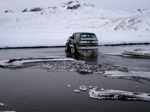 1996 Ford Bronco - A 1996 Ford Bronco navigates a shallow, partially frozen river in a snowy landscape.