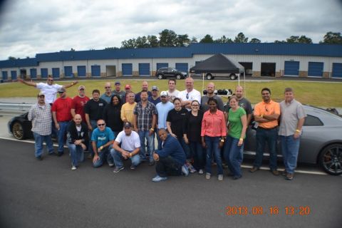 1979 Ford F-150 - A group of people gathered for a photo at a motorsports park with a sports car in the background.