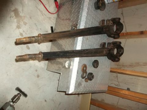 1995 Ford Bronco - Two rusty front axle beams with spindles are laid out on a metal surface, possibly for restoration.