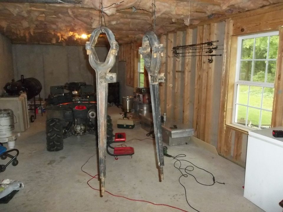 Two large metal suspension components hanging from wires in a garage. An ATV is visible in the background