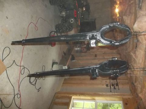 1995 Ford Bronco - Two large black metal axles are laid out on a garage floor, with fishing rods hanging nearby.