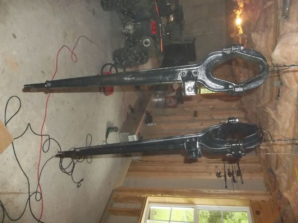 two black metal axles with clamps on one end, on a concrete floor