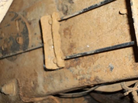 1995 Ford Bronco - The underside of a vehicle shows heavily rusted metal components and brake lines.