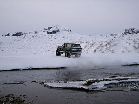 1996 Ford Bronco - A lifted green Ford Bronco navigates a snowy, icy landscape with a body style consistent with the early to mid-1990s.