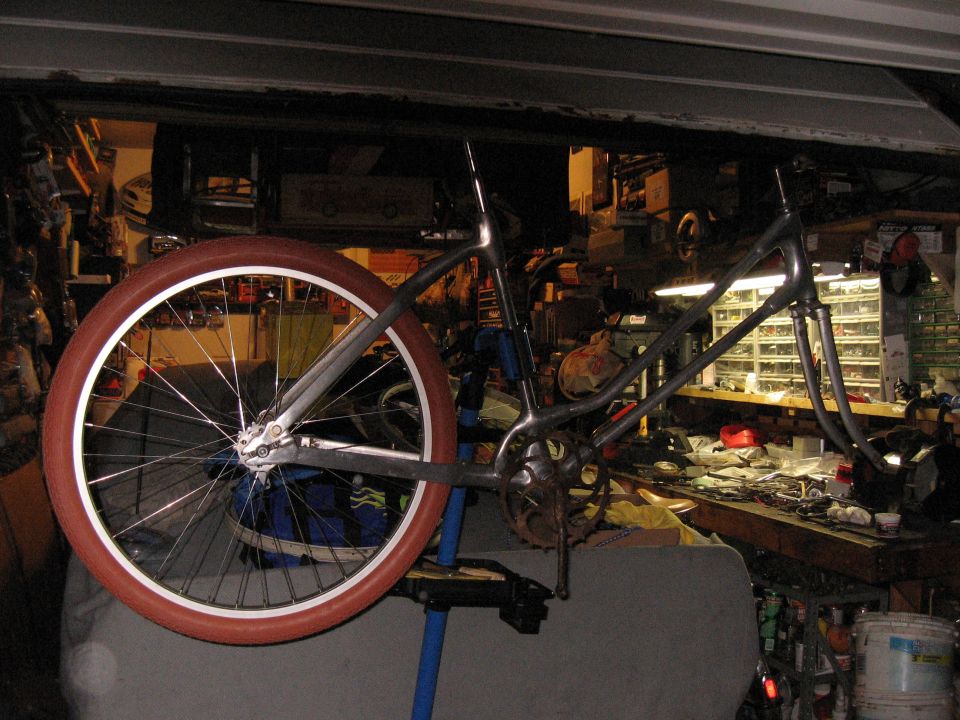 Bicycle frame with one red-walled wheel on a stand in a cluttered garage