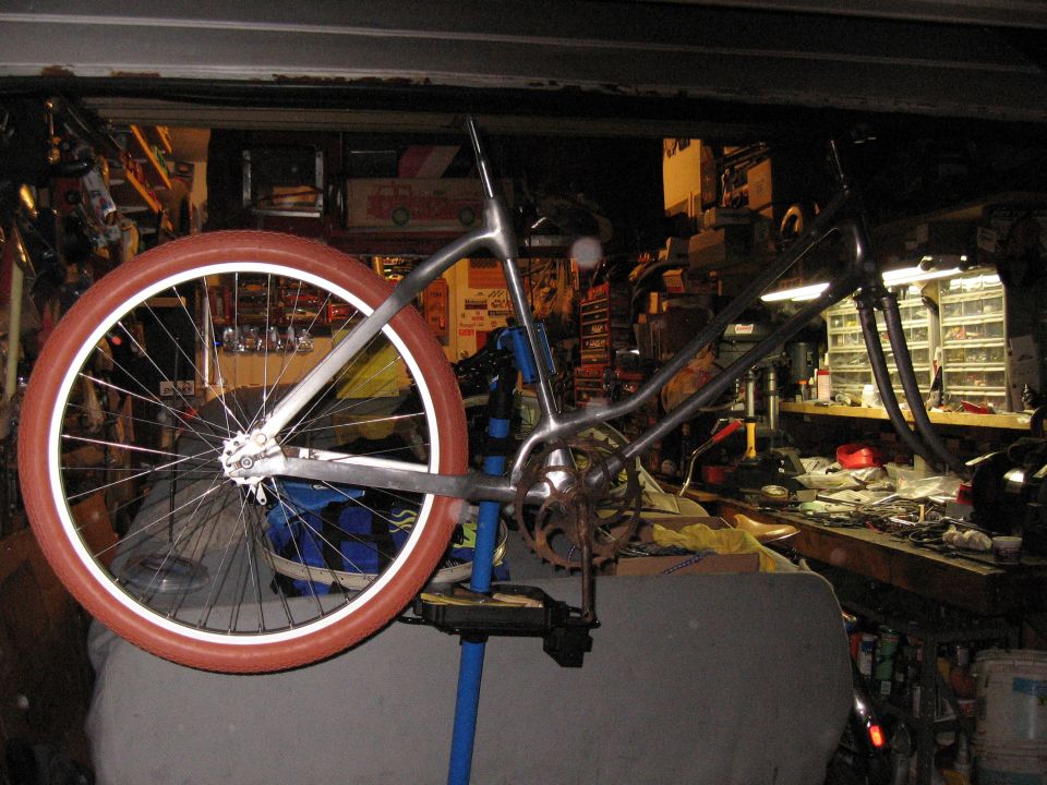 Bicycle frame with one red-walled wheel on a blue repair stand in a cluttered garage