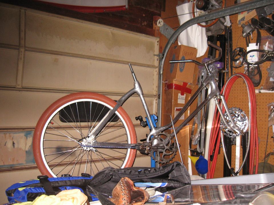 Chrome bicycle frame with a large, tan tire and spokes, leaning against a garage wall