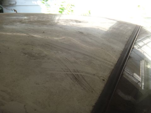 1990 Ford Taurus - The dusty surface of a car's roof shows streaks and smudges, with sunlight reflecting off the glass.