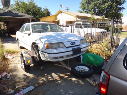 1990 Ford Taurus - A white 1990 Ford Taurus is on a trailer, with a person working on its underside.