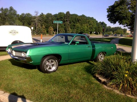 1971 Ford Ranchero - A green Ford Ranchero with racing stripes sits parked on a lawn beside a white trailer.