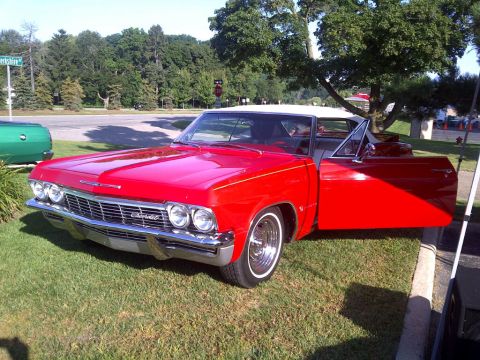 1971 Ford Ranchero - A red 1965 Chevrolet convertible with its doors open, parked on a grassy area next to a road. The Chevrolet badge is visible on the front g…