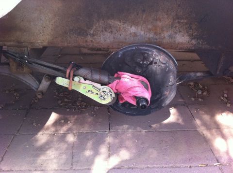 1999 Ford F-250 - A trailer brake drum is secured with a ratchet strap and a pink cloth, resting on a paved surface.