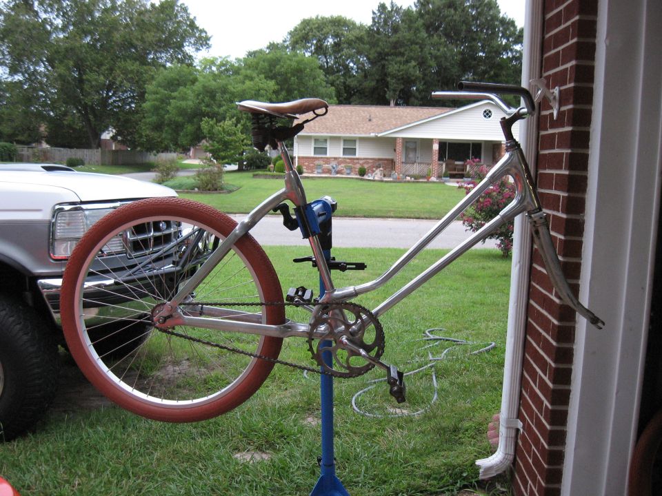 Silver bicycle frame with red tire on blue stand, parked next to a white truck