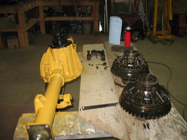 Yellow painted differential assembly and two dark metal differential gears on a wooden workbench