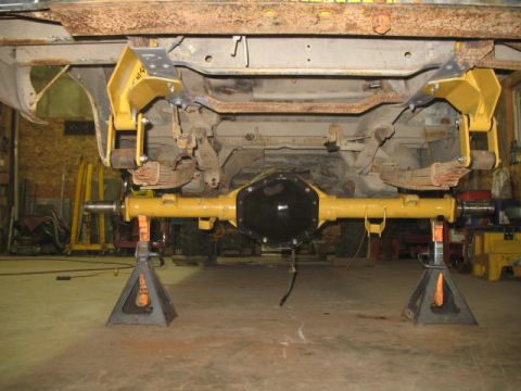 1989 Chevrolet C/K Pickup - Underside view of a rear axle assembly, painted yellow and supported by jack stands, undergoing work.