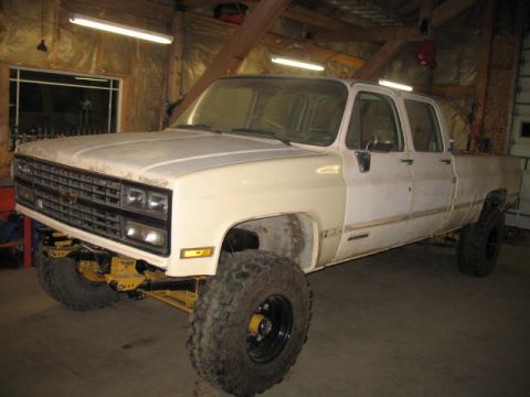 1989 Chevrolet C/K Pickup - This lifted pickup truck is in a garage, possibly undergoing modifications or repairs.