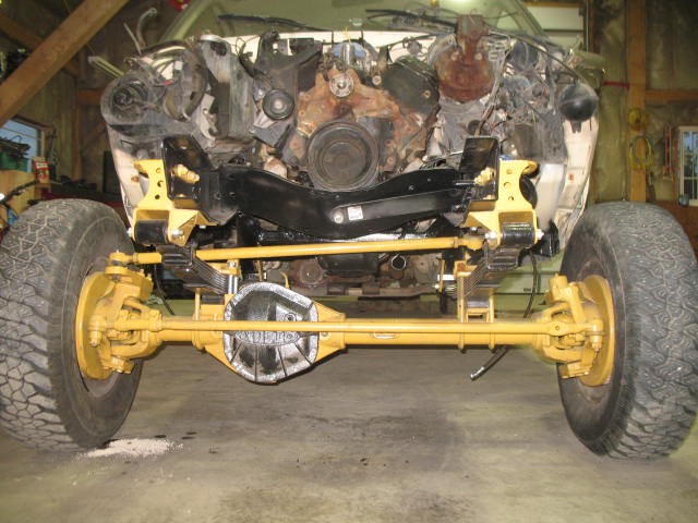Front axle, suspension, and engine of a truck undergoing repair. Yellow painted components are visible