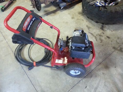 1995 Ford Bronco - A red Troy-Bilt pressure washer sits on a concrete floor, with a large tire and vehicle parts in the background.