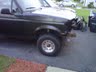 1994 Ford Bronco - A dark-colored SUV, possibly a Ford Bronco, is parked outside with visible front-end damage.