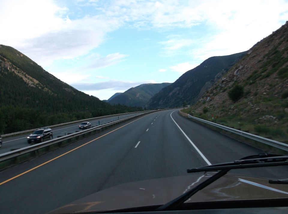 View from a vehicle driving on a highway through a mountainous area, with other cars on the road