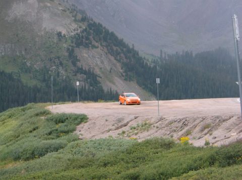 2009 Kenworth T800 - An orange hatchback is parked on a dirt road with a mountainous landscape behind it.