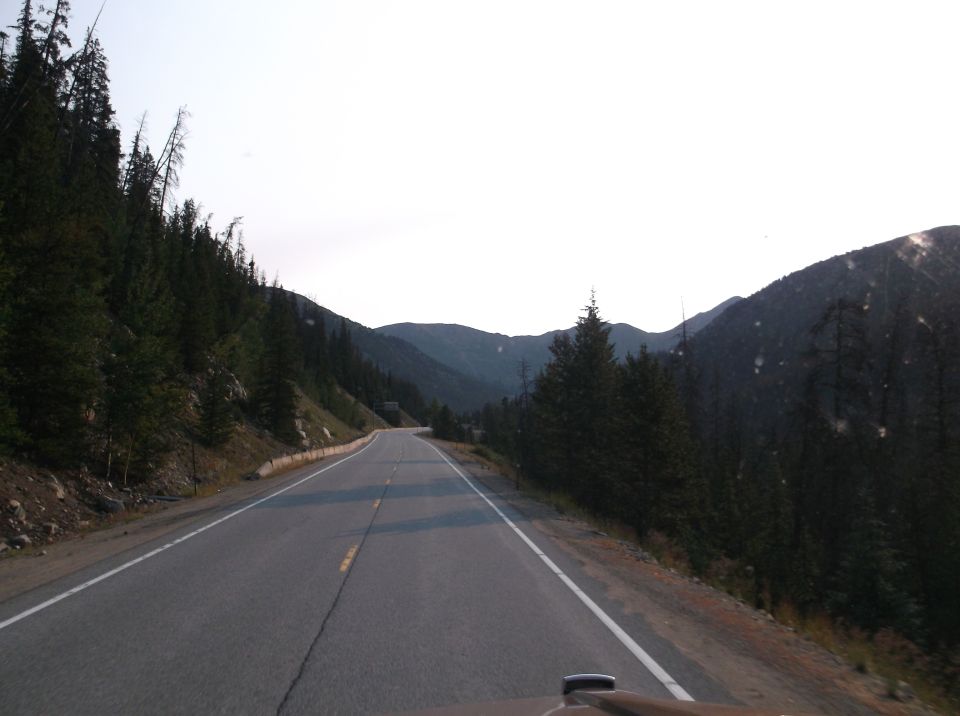 Driving on a two-lane road through a mountain pass with pine trees and overcast sky
