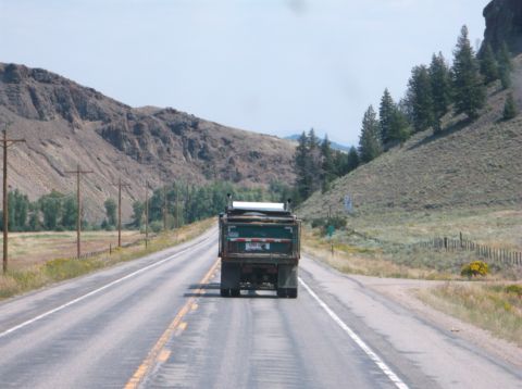 2009 Kenworth T800 - Dump truck travels down a two-lane highway through a mountainous landscape.