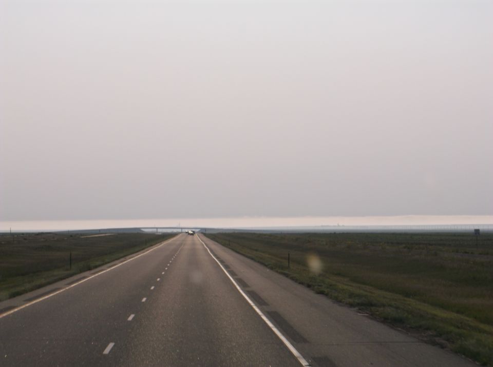 long highway stretching into hazy distance with a few cars far ahead