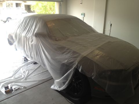 2013 Ford Mustang - A vehicle is covered in plastic sheeting inside a garage, with tools visible on the floor.