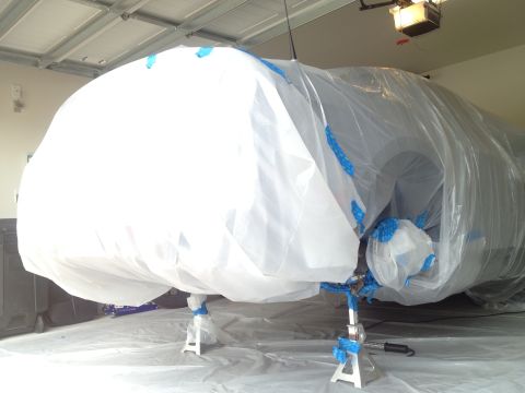 2013 Ford Mustang - A vehicle is covered in protective sheeting and plastic in a garage, obscuring its details.
