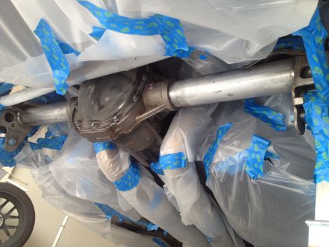 2013 Ford Mustang - The rear axle and exhaust system are covered in plastic sheeting and blue painter's tape, likely in preparation for painting or detailing.