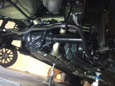 2013 Ford Mustang - The underside of a vehicle is shown, detailing the rear axle, suspension components, and exhaust pipes, with the car elevated on jack stand…