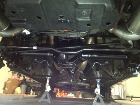 2013 Ford Mustang - The underside of a 2013 Ford Mustang reveals its rear axle, suspension components, and exhaust system, all elevated on jack stands.