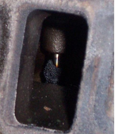 1980 Ford Bronco - A close-up view of an engine component reveals a metal rod protruding into a cavity filled with dark debris.